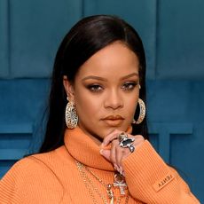 Rihanna wears a long-sleeved orange dress, large diamond hoop earrings, and has long straight black hair