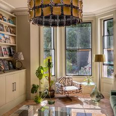 Bay window with floor lamp, armchair covered in abstract pattern, glass coffee table and houseplants by built in bookshelf area