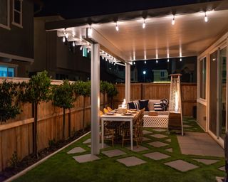Patio at night with pavers mixed with artificial grass, a seating area and lights