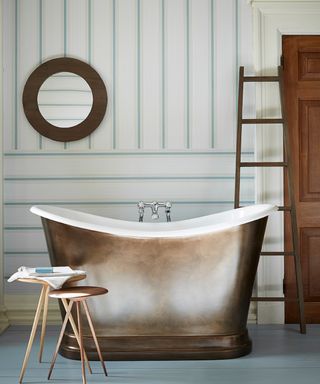 Coastal bathroom with striped wallpaper and freestanding metal bathtub