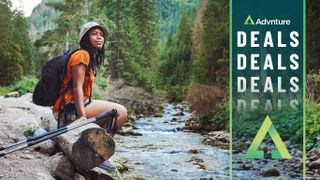 Woman with trekking poles pausing by stream