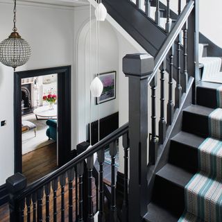 Staircase with dark grey banisters and treads, central lights hanging through the centre and framed pictures on the wall