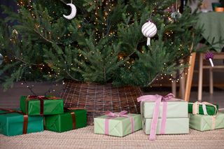 A close up of Christmas presents round the base of a Christmas tree with a dark brown, wicker tree skirt.