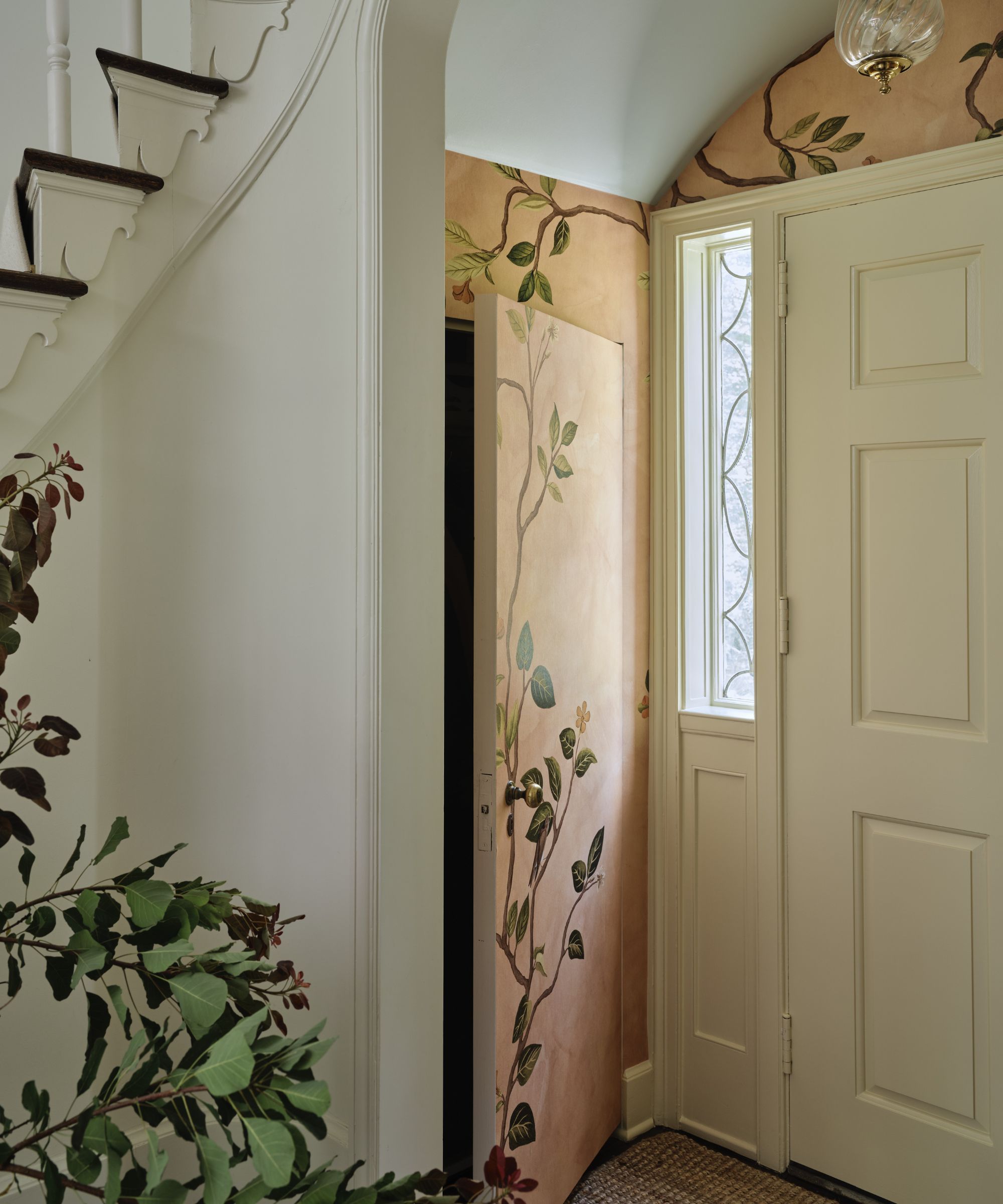 a calm neutral entryway with pink floral mural painted around the front door with a side door to a hidden cupboard