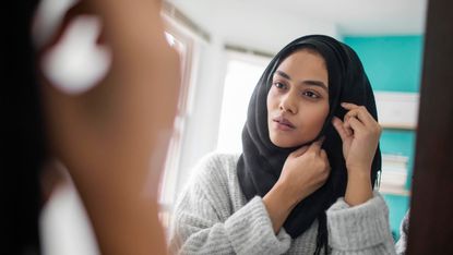 woman wearing hijab looking at herself in the mirror