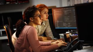 Two female workers looking at screens of computer code