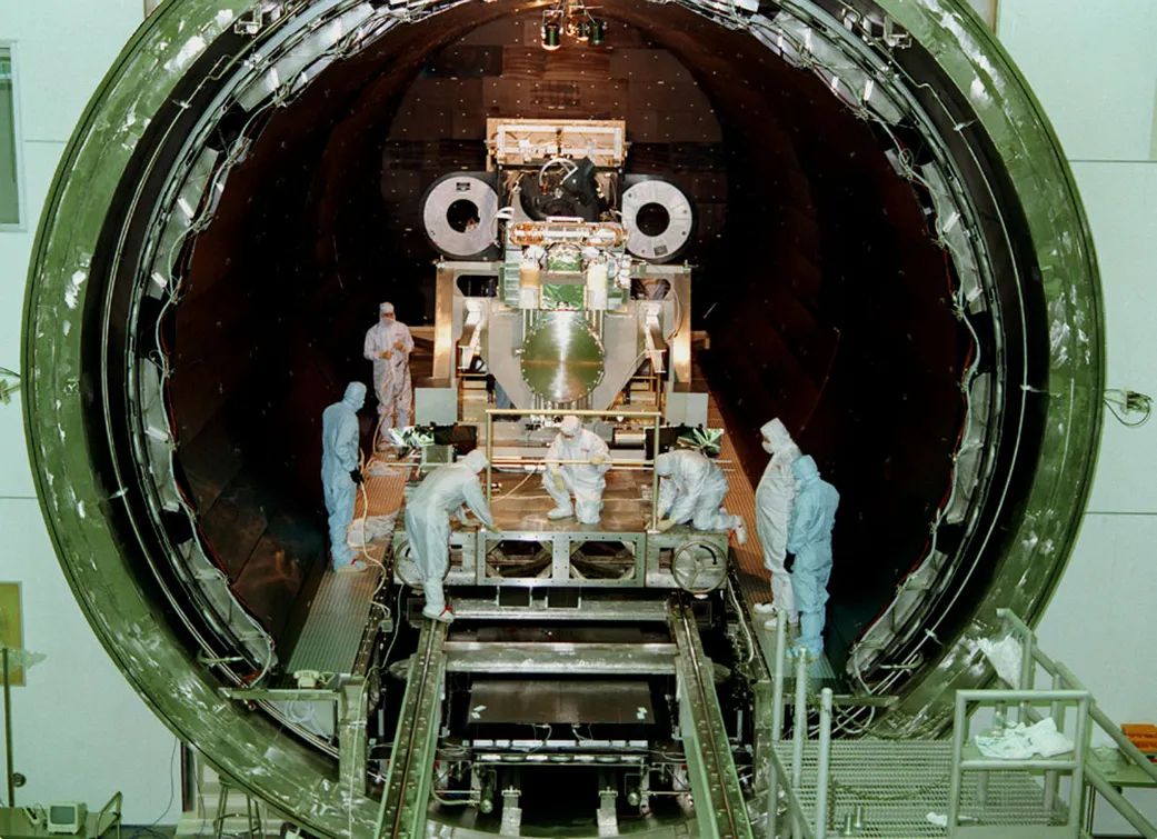 Technicians in clean suits inspect large machines in a circular doorway several metres across.