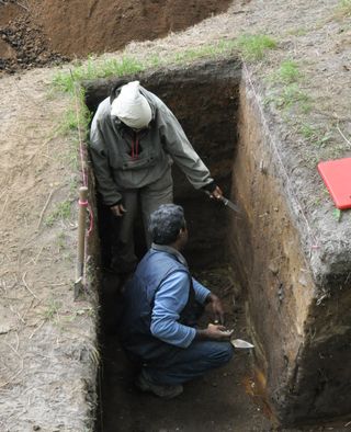 Scientists crouch at an excavation where they are studying sediment layers in the Russian Far East to look for signs of past seismic hazards.