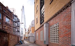 View of Gibbon's Rent alley during the day. There are multiple buildings, a brick wall with a metal deterrent on top and a view of The Shard in the distance