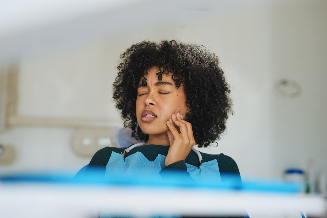 Tooth sensitivity: A woman holding her hand to her jaw in apparent pain while sitting in a dentist's chair.