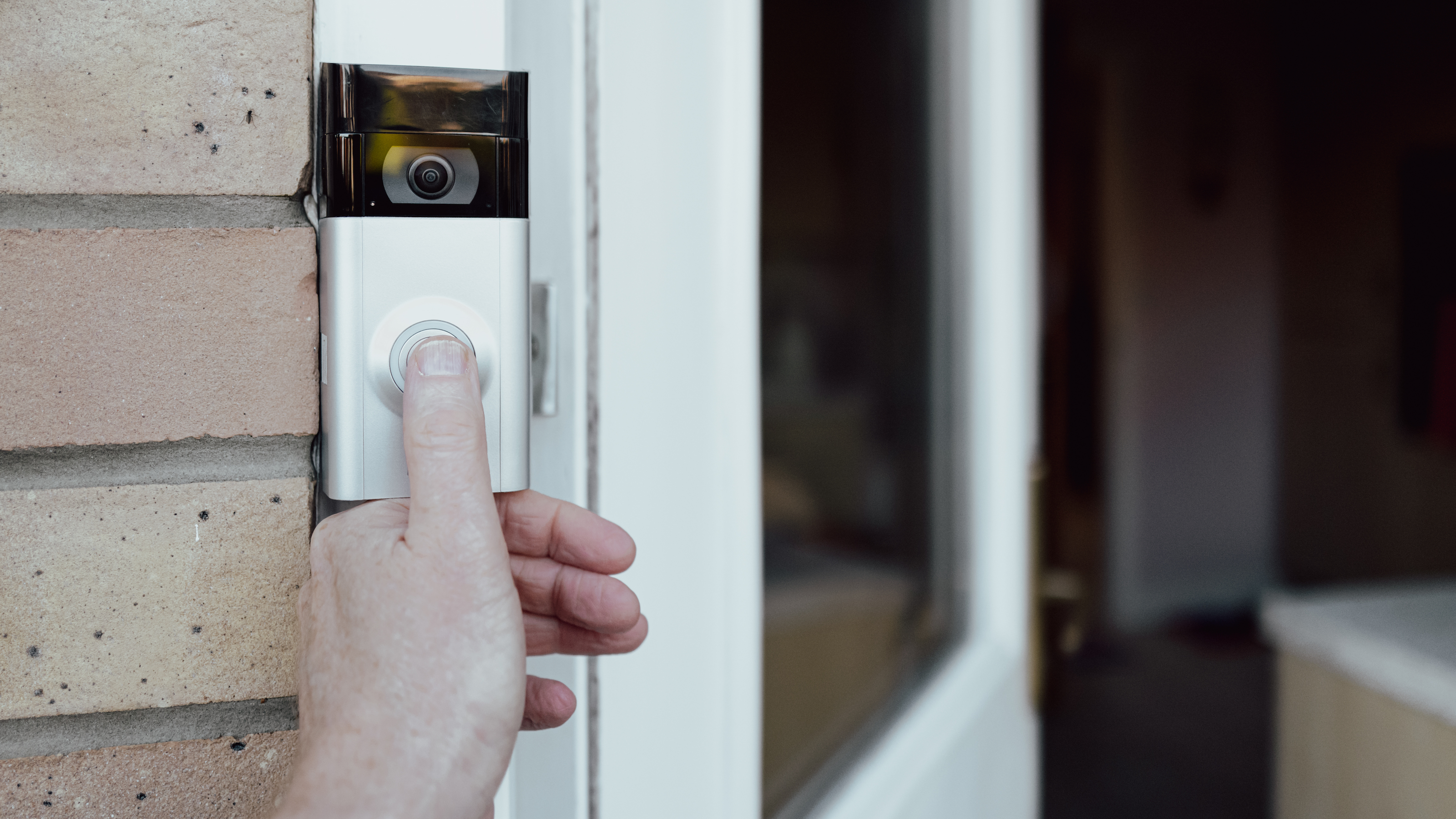 Person’s hand pressing button to test video doorbell fitted alongside white door