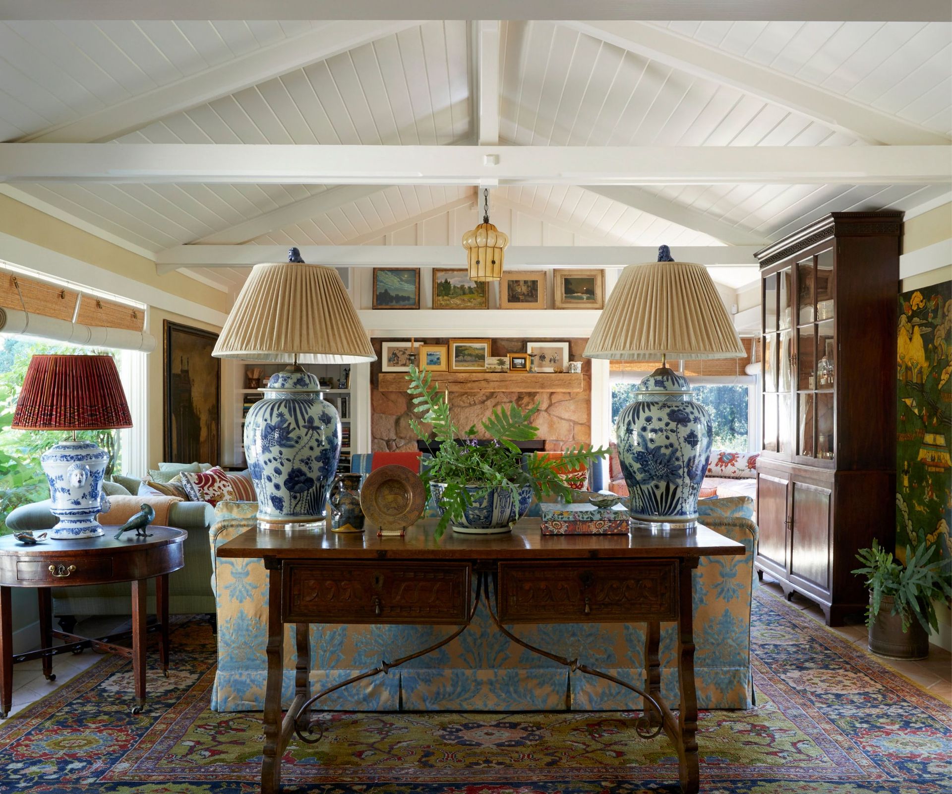 Eclectic living room with console with two blue and white antique lamps, Persian rug and white wood panelled ceiling