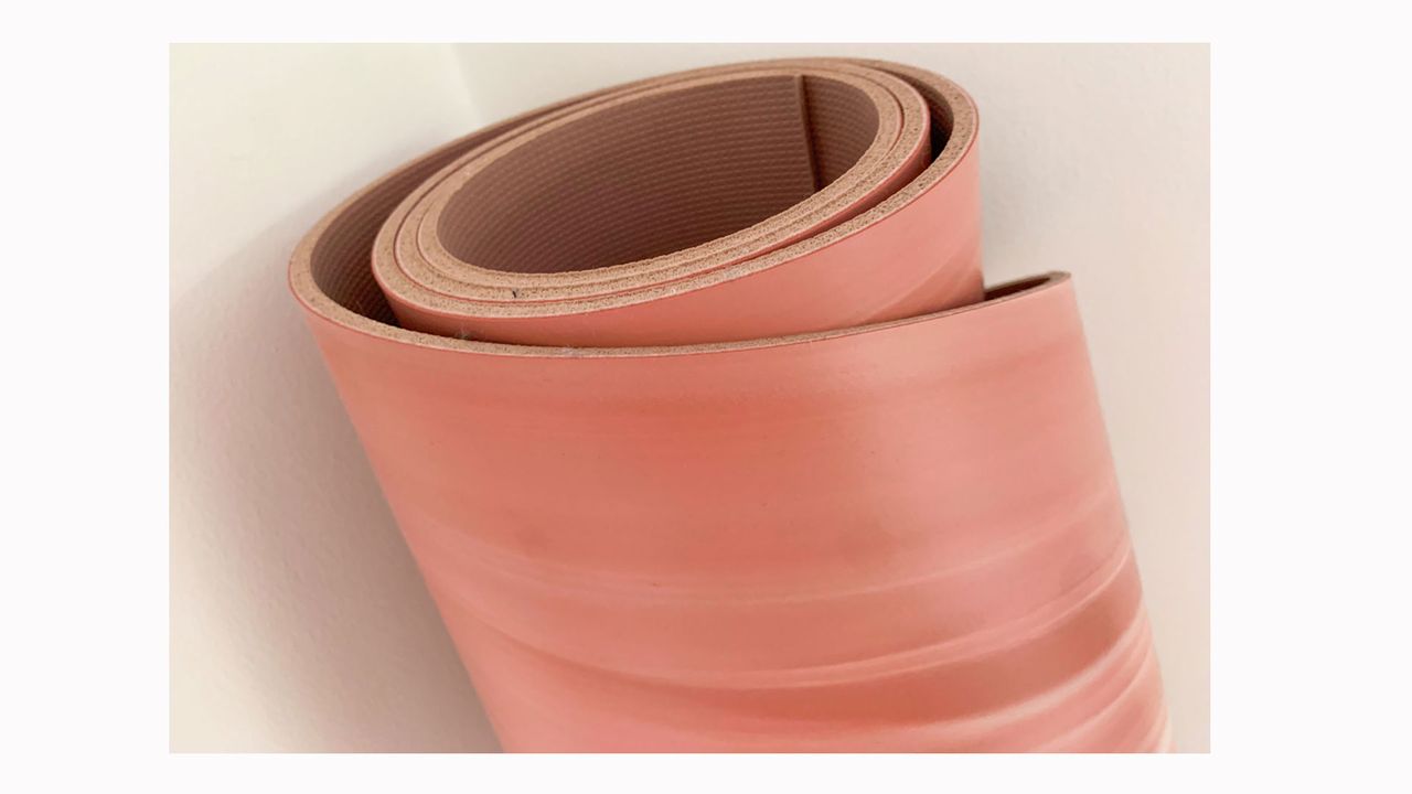 Image is a closeup of a pink rolled up Lululemon Reversible 5mm Yoga Mat.