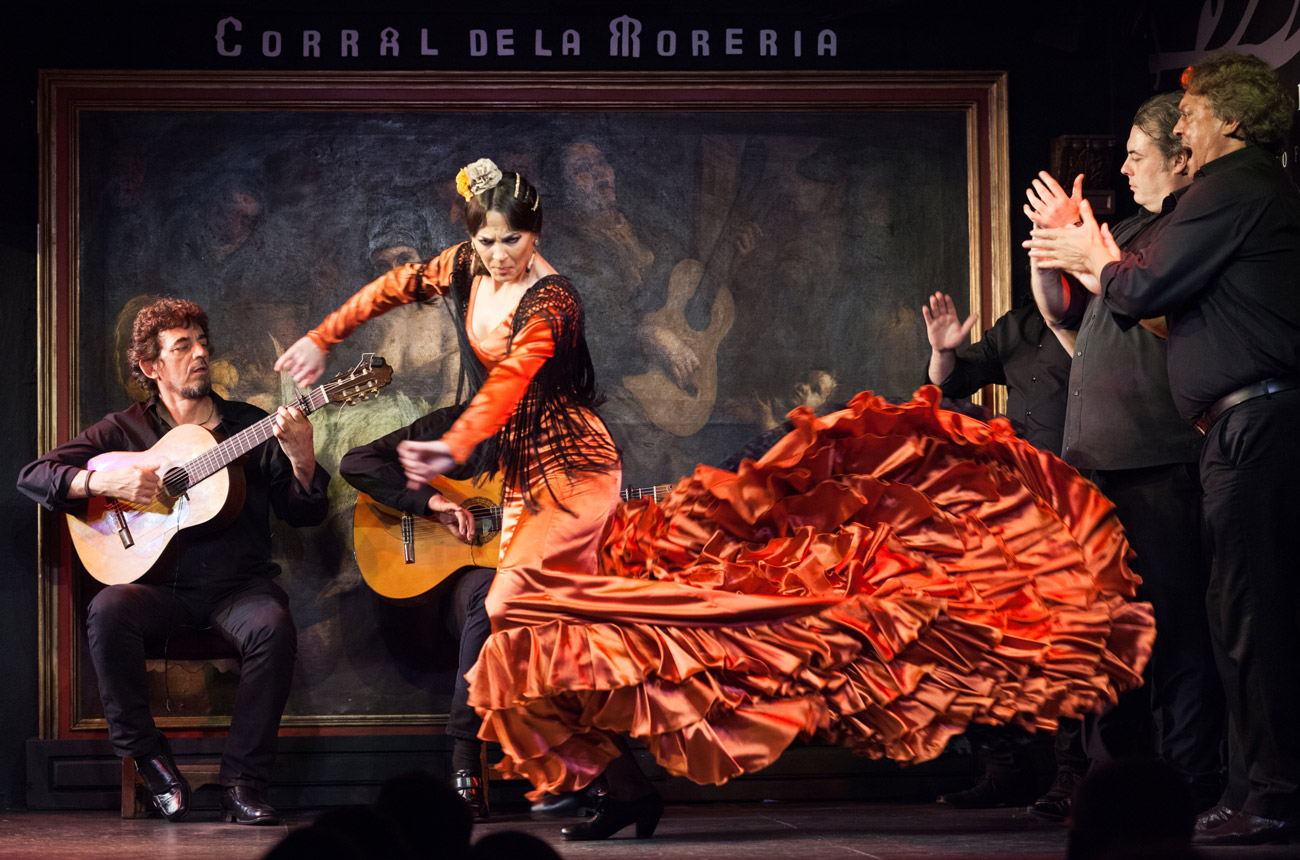 A woman in a red dress dancing flamenco surrounded by musicians
