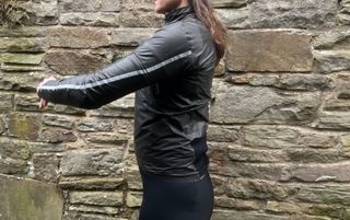 This is an image of a woman standing in front of a stone wall facing to the right with her arms in front of her. She is wearing the Castelli Idro 3 women's jacket.