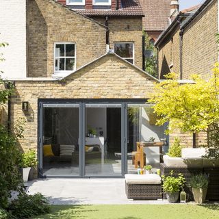 brik house with glass black paneled doors and outside furniture next to trees and plants