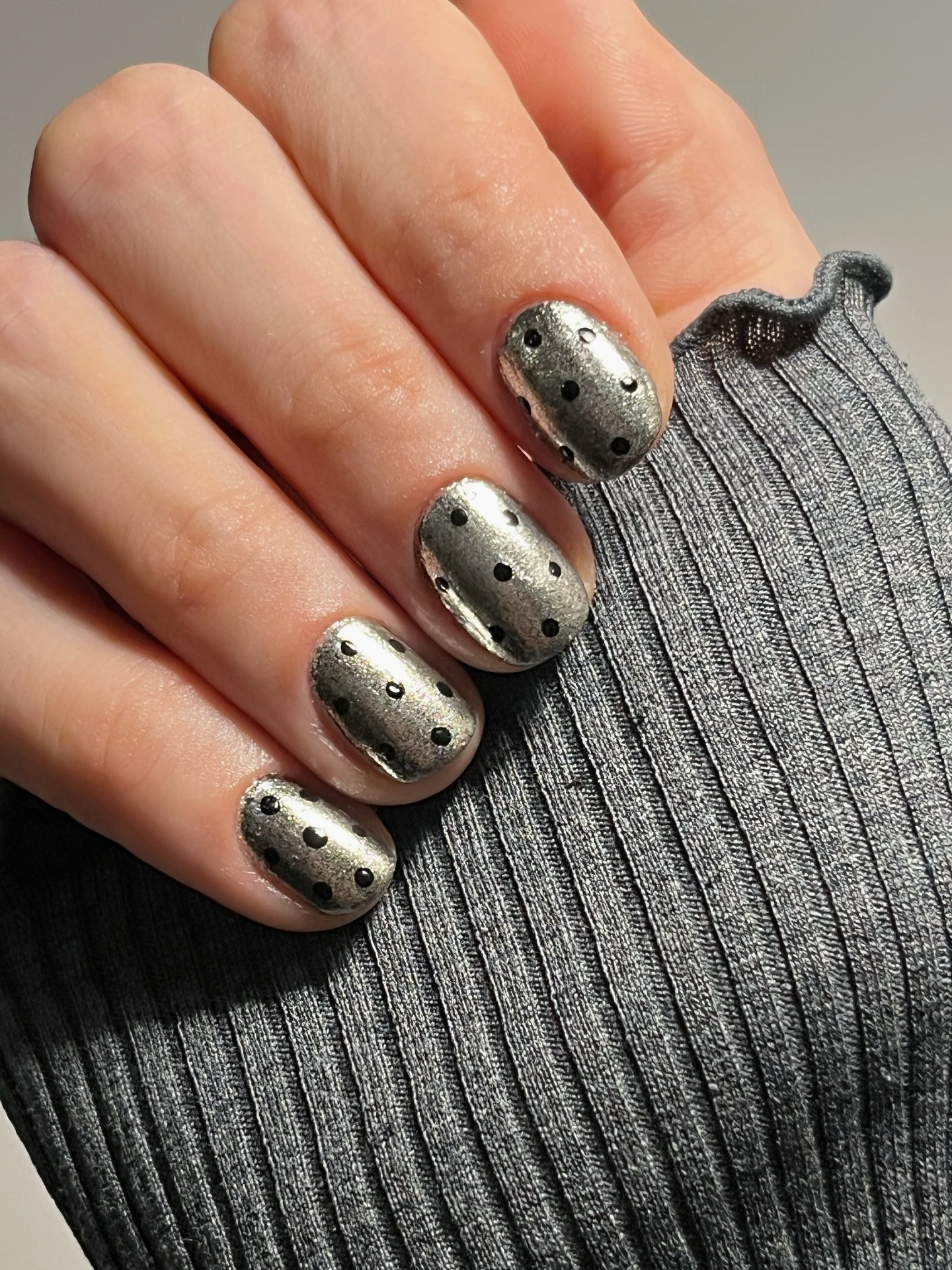 A silver chrome manicure with black polka dots