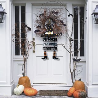 White front door with Halloween decorations, pumpkins and branches