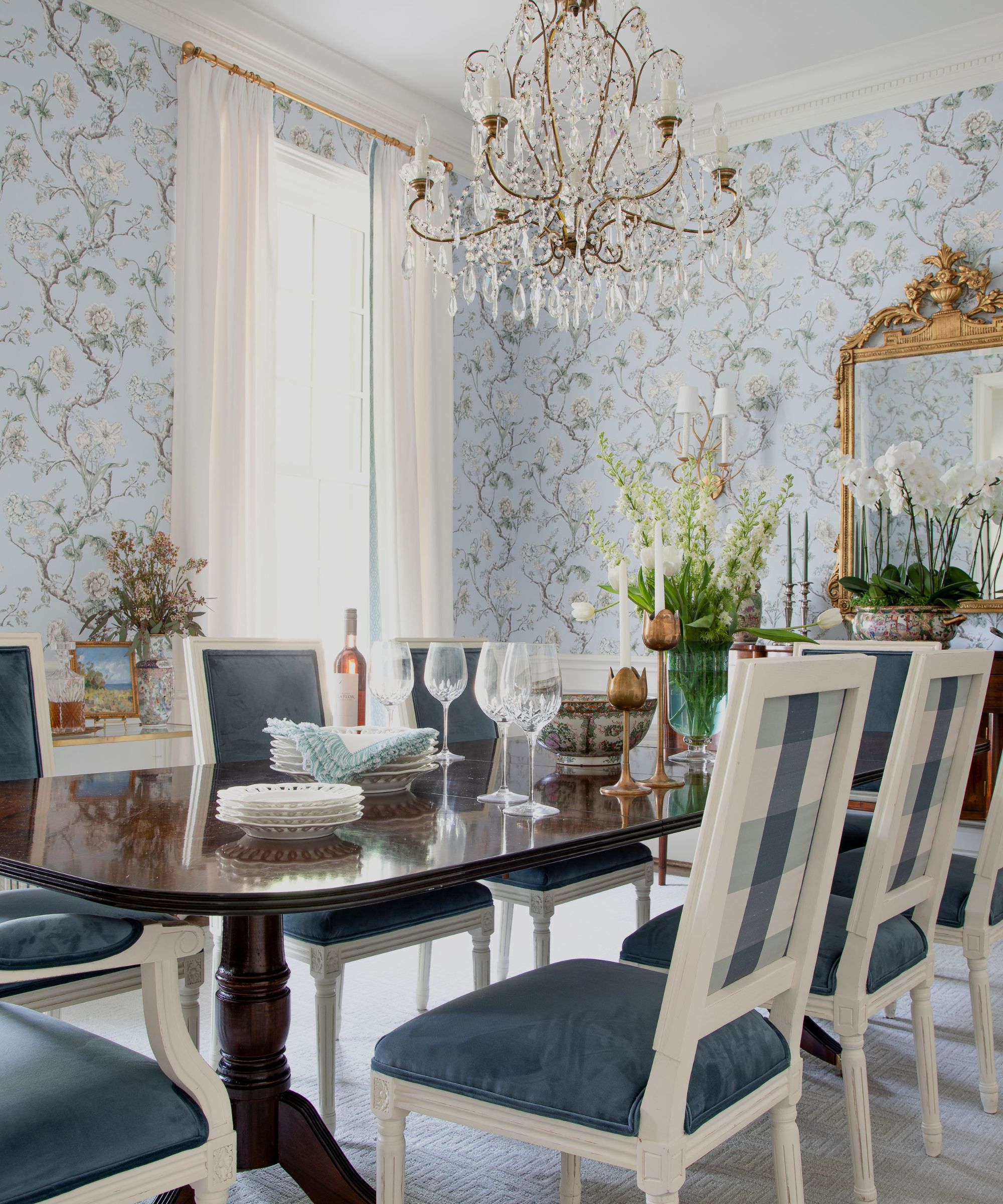 Dining room with pale blue floral wallpaper, dark wood dining table, blue chairs and chandelier