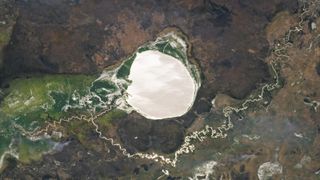 A satellite photo of a large, rounded lake shining like a mirror alongside a windy river