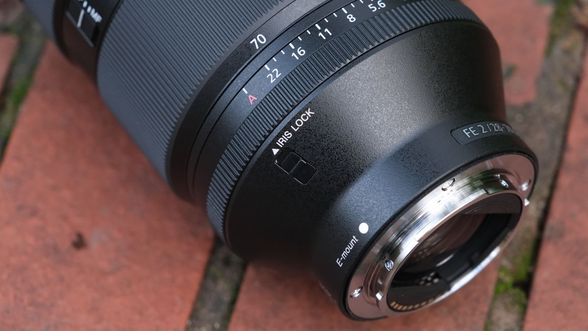 Close up of the iris lock switch on a Sony FE 28-70mm f/2 GM lens on a brick wall