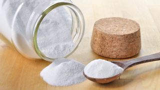 A spoonful of baking soda next to a spilled jar and a cork lid