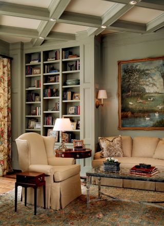 Study with armchair and sofa, wood floor with rug, bookshelves, wall and ceiling coffers in teal, and neutral armchair and sofa