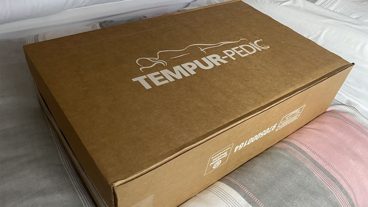 The cardboard box the Tempur-Pedic Tempur-Cloud pillow was delivered in, with the Tempur-Pedic logo on top, sitting on a bed in our reviewer's home