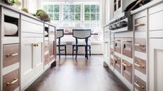 An image of a kitchen walkway with white cabinetry on either side with wooden inset drawers with brass hardware