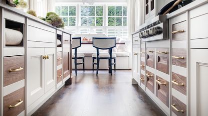 An image of a kitchen walkway with white cabinetry on either side with wooden inset drawers with brass hardware 