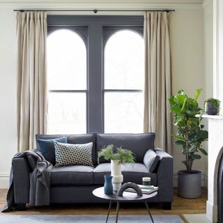 Off white living room with arched windows with the frames painted mid grey to match a grey sofa in front of them
