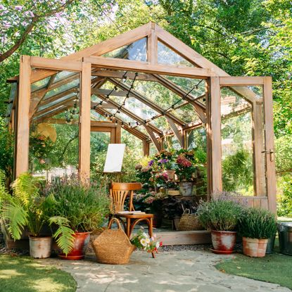 Wooden greenhouse in garden with seat and potted plants