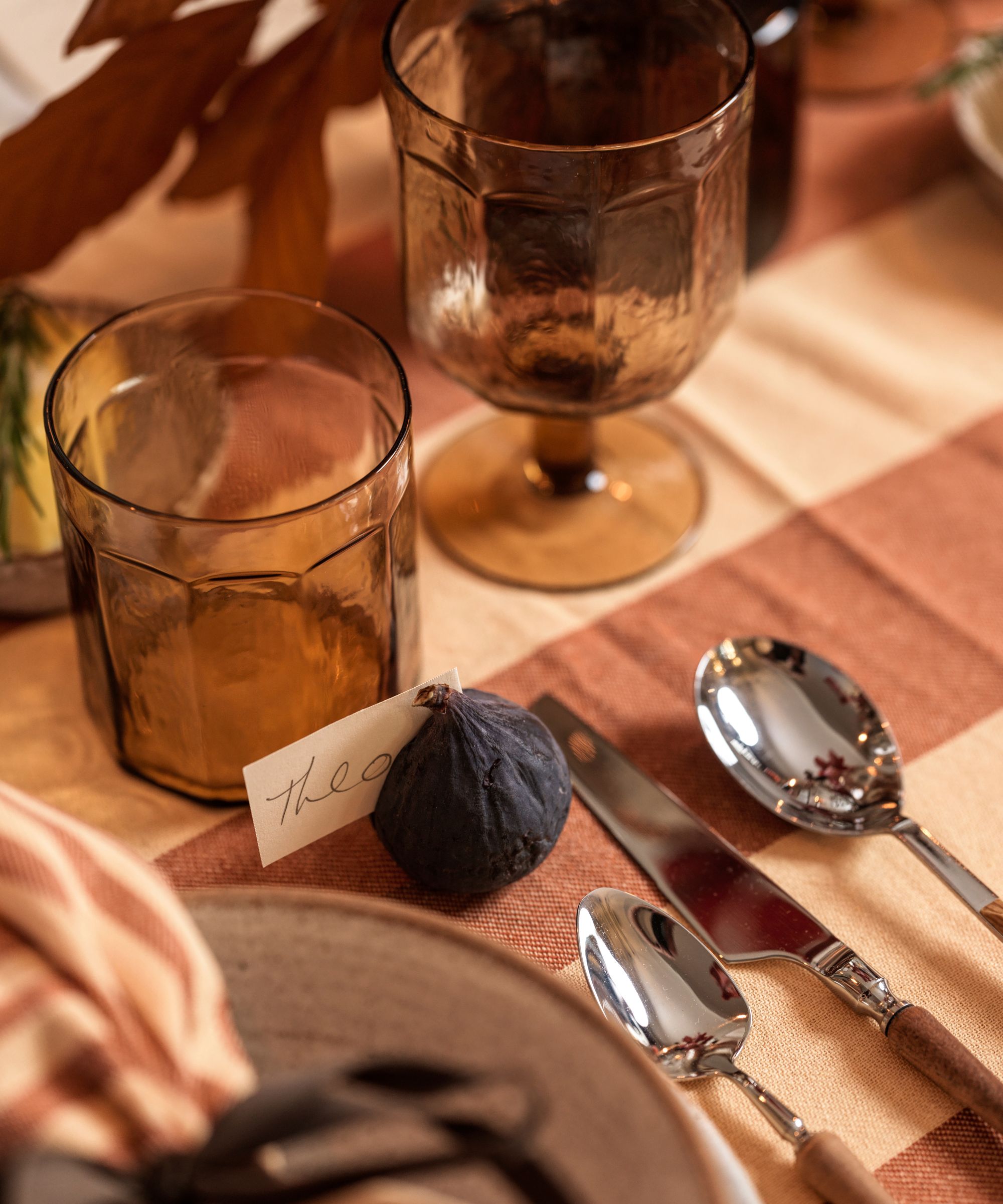 Tablescape with amber glassware, brown and cream striped tablecloth, and fig place card holders