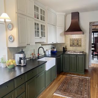 A kitchen with green cabinetry, wooden floors, and a copper oven hood