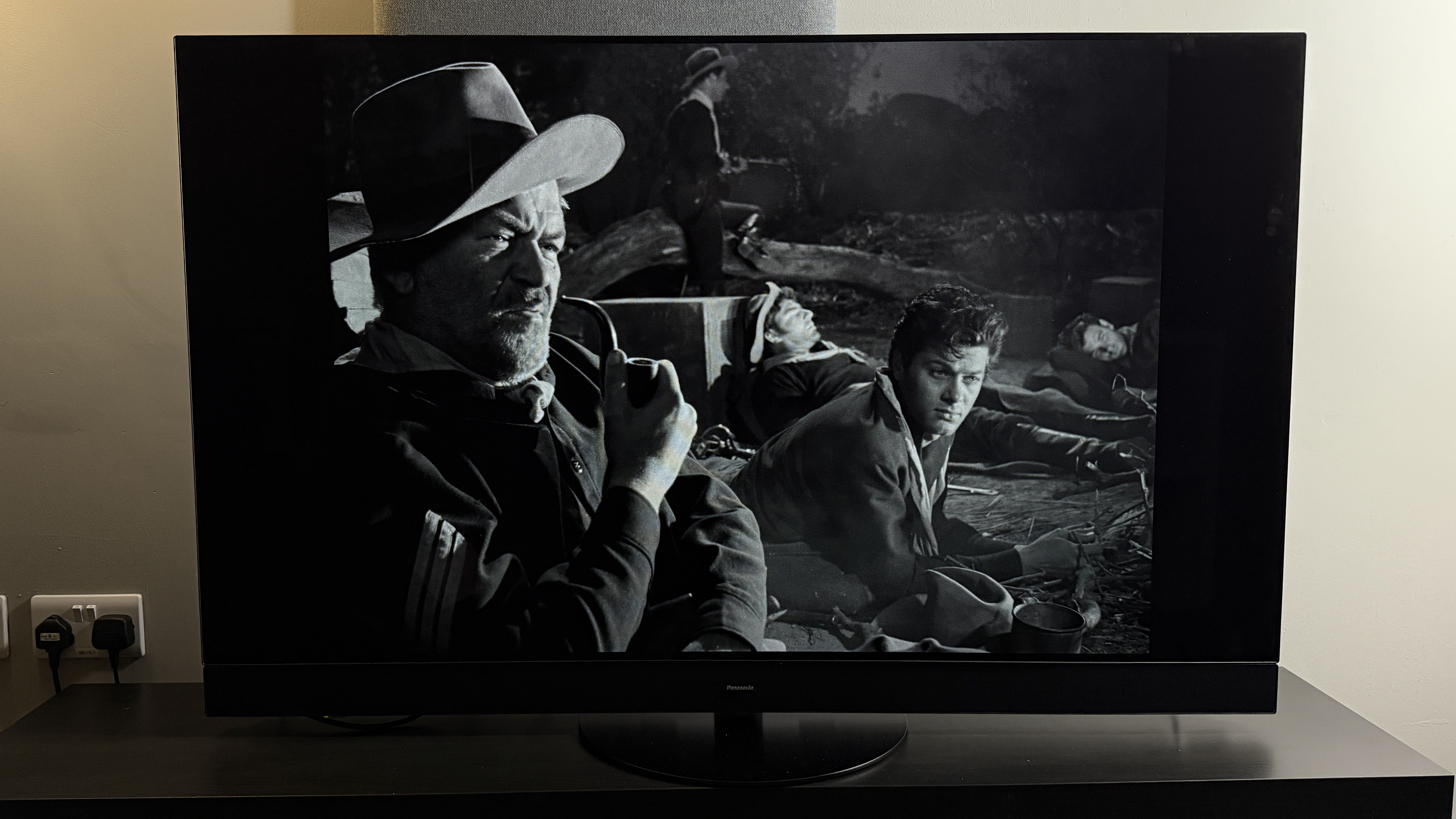 A TV showing the movie Winchester '73, a man smokes a pipe in the darkness on-screen