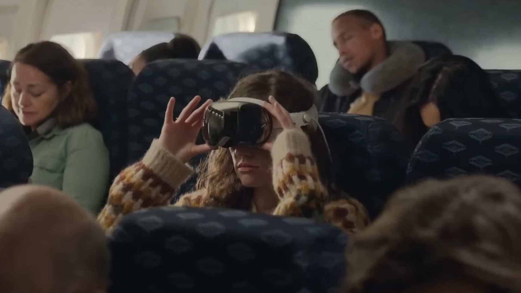 A woman wearing the Apple Vision Pro while on a plane with other passengers next to them.