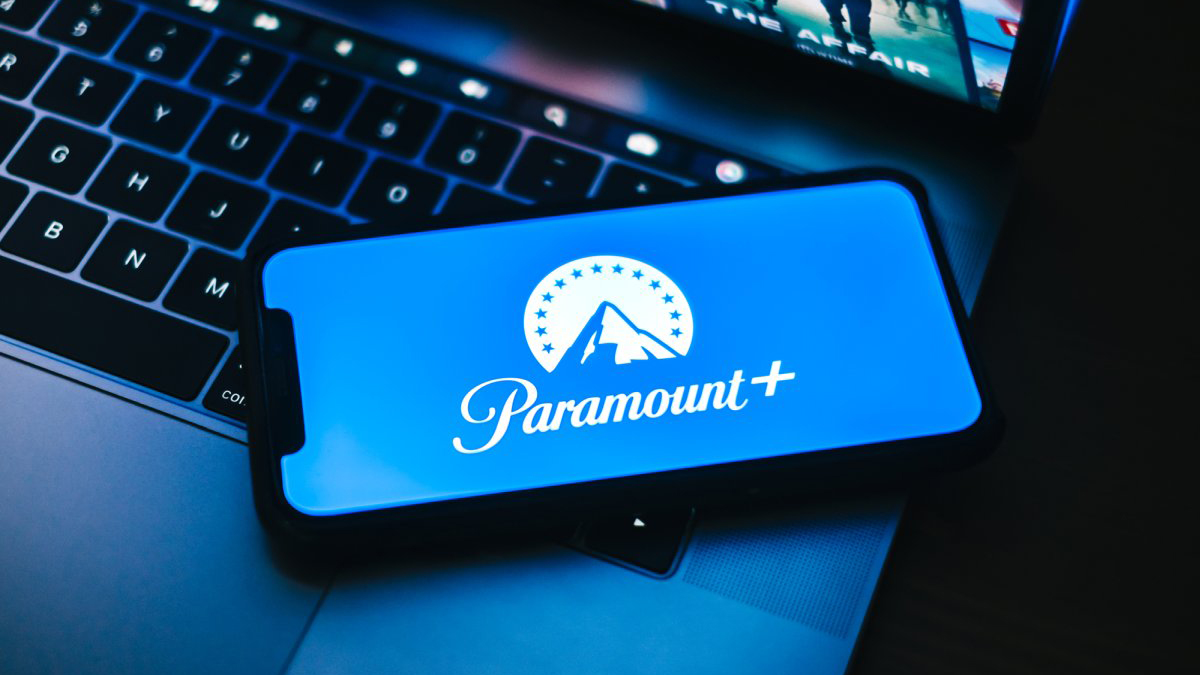 تصویر آرم Paramount Plus در تلفن همراه که روی لپ تاپ قرار دارد