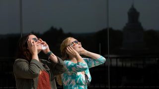 Two women observe the sun with solar eclipse glasses at SUNY Potsdam university.