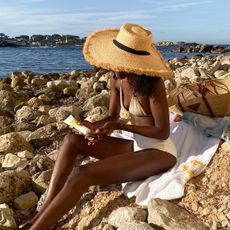 A woman sitting at the beach wearing a white bikini set and a large straw hat. 