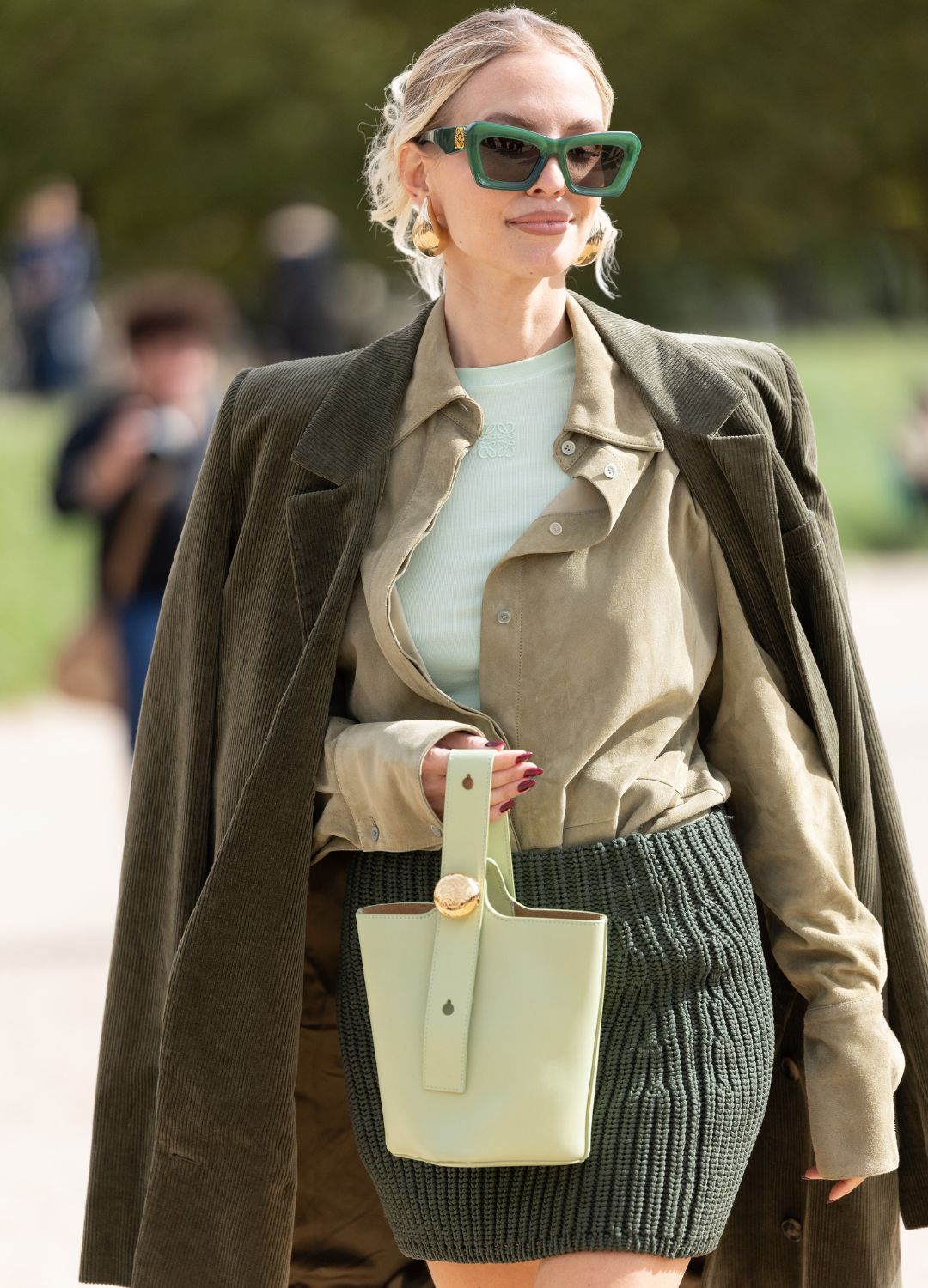 Leonie Hanne wears gold earrings, green feather heeled sandals, green sunglasses, a light green suede shirt, a mint green t-shirt, a dark green mini skirt, a mint green leather bag and a military green jacket outside Loewe show during Womenswear Spring/Summer 2025 as part of Paris Fashion Week on September 27, 2024 in Paris, France.
