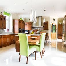 kitchen area with wooden kitchen units and white wall and dining table with green chairs