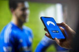 Die NordVPN App auf dem Handy, im Hintergrund ein Fußballspiel auf dem TV