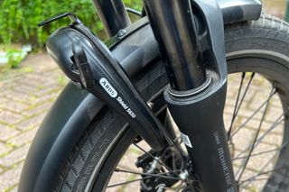 This image of the Tern GSD S10 shows a close up of the integrated front ABUS Shield 5650 lock, also in the image are the Suntour suspension forks, and front wheel with mudguard.