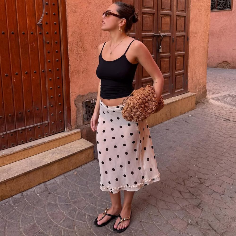 @oliviagraceherring wears a white and black polka dot skirt with a black tank, flip-flops and raffia tote