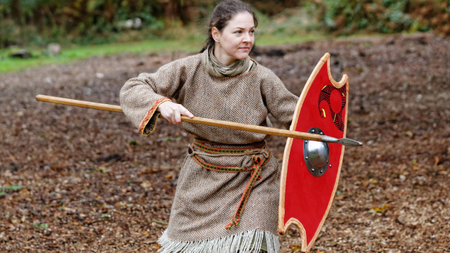 A woman wears a costume and holds a shield and spear