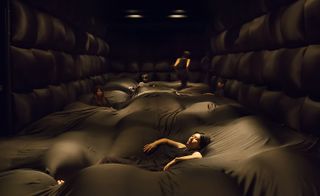 A dark room covered in brown cushions and people relaxing.