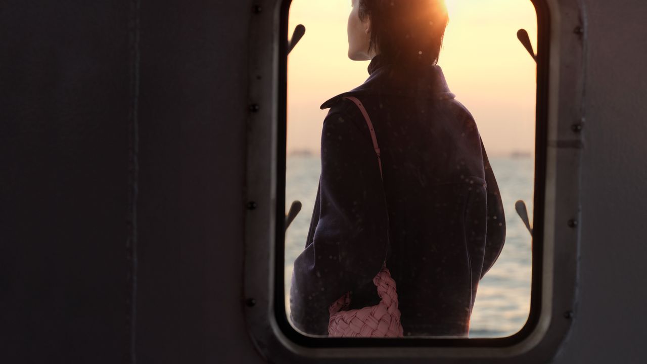 Woman stands on outside of window in Bottega Veneta video, holding pink bag