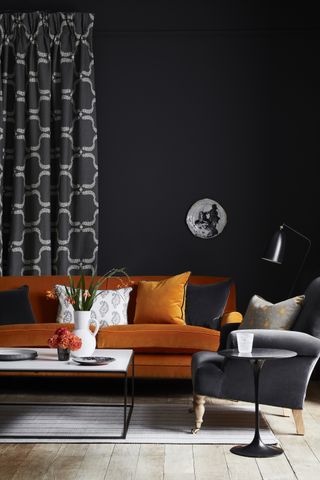 An orange velvet sofa in black living room by Vanessa Arbuthnott with grey armchair and grey and white patterned curtain