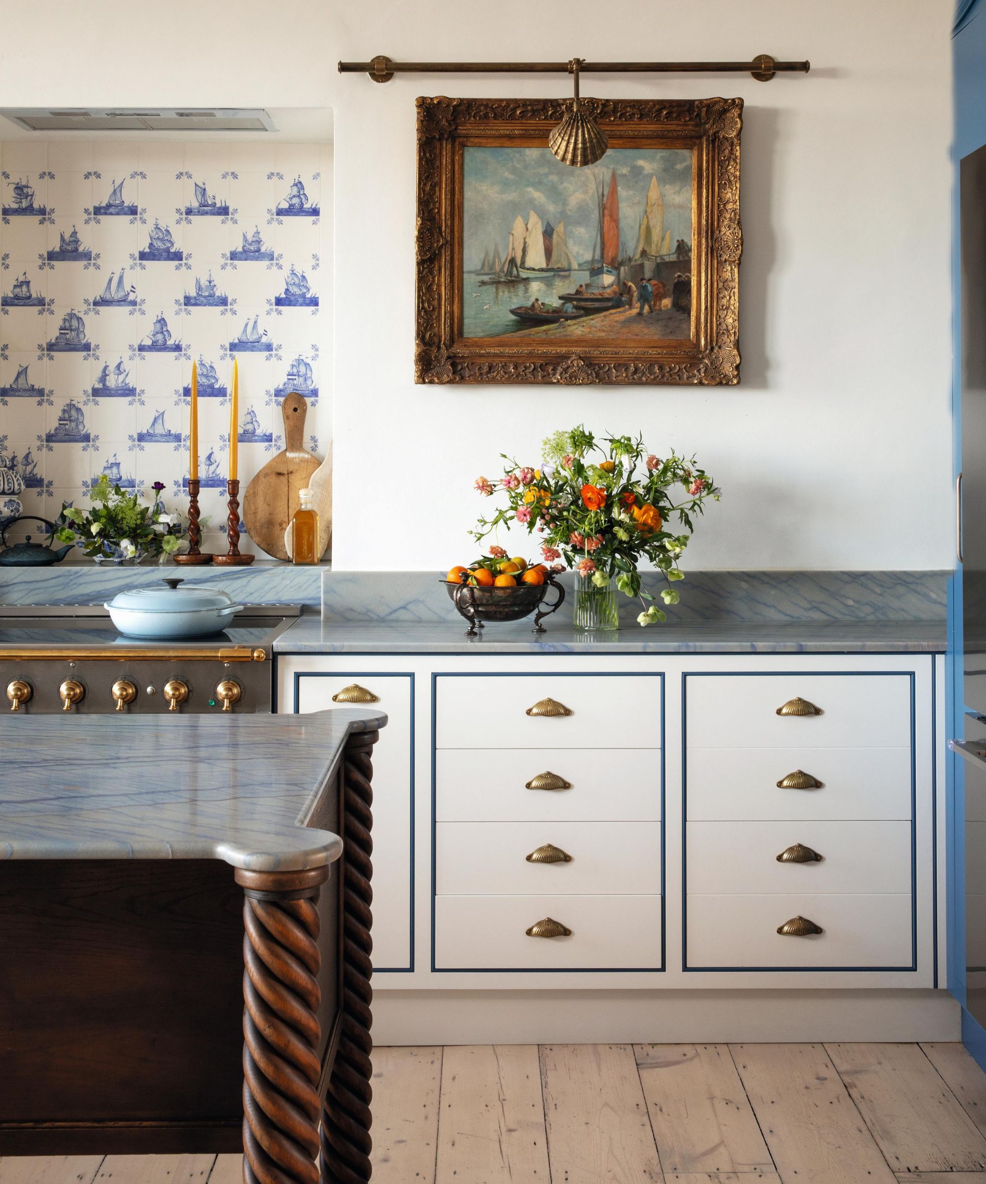 a white kitchen with white and blue cabinetry, a large coastal antique painting and a blue marble countertop
