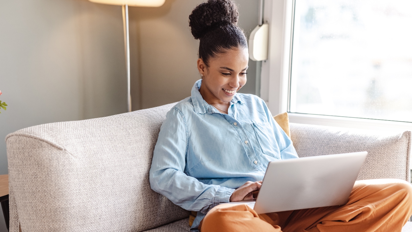 Woman sitting on the couch with a laptop in her lap smiling at it
